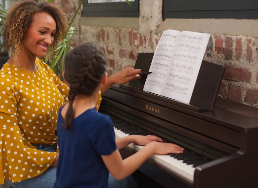 Hình ảnh người phụ nữ đang học đàn piano Kawai CA501 R cùng một bé gái
